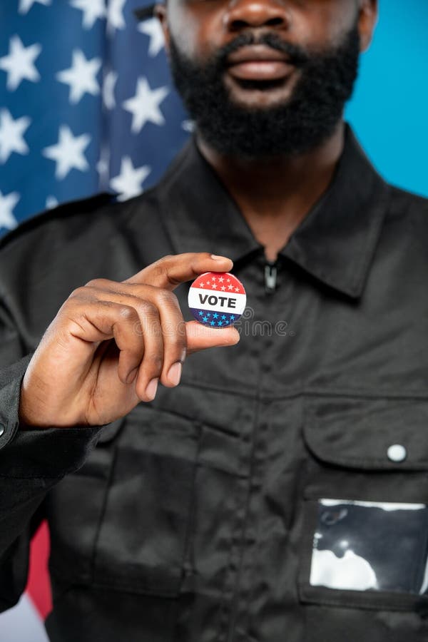 Main de sécurité mâle africaine en uniforme à barbe noire montrant les insignes de vote