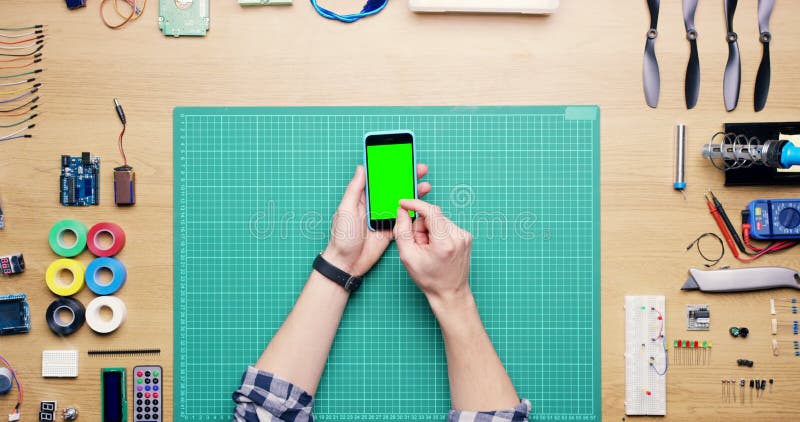 Main de technicien et défiler sur un téléphone à écran vert avec outils sur le bureau pour l'ingénierie informatique ou matériel. banque de vidéos