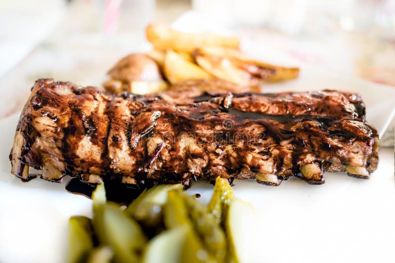 Main dish at fancy restaurant - american pork ribs on barbeque sauce with pickels and oven potatoes stock photography Main dish at fancy restaurant - american pork ribs on barbeque sauce with pickels and oven potatoes stock photography