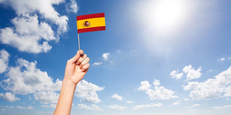 Main du ` s de femme tenant le drapeau espagnol contre le ciel bleu photos libres de droits Main du ` s de femme tenant le drapeau espagnol contre le ciel bleu photos libres de droits