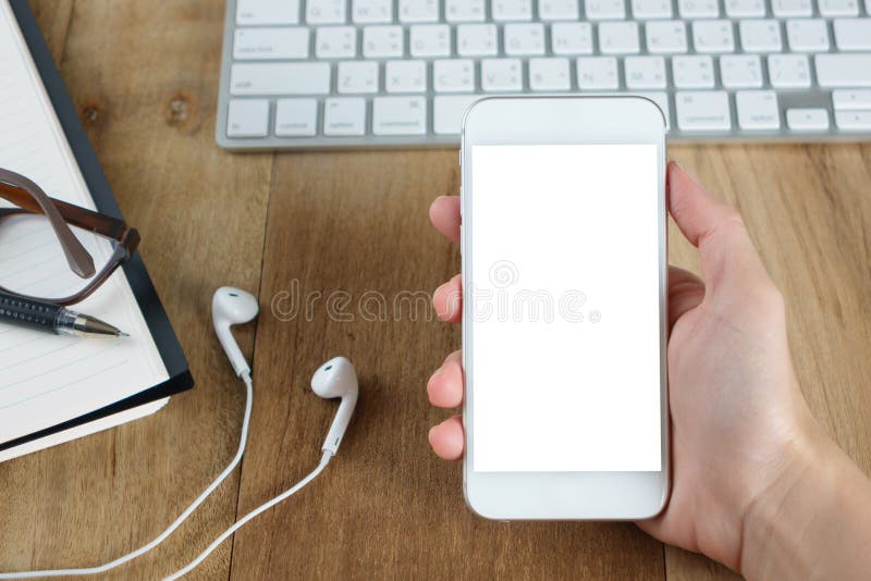 Main du ` s de femme tenant le smartphone sur le bureau fonctionnant image stock Main du ` s de femme tenant le smartphone sur le bureau fonctionnant image stock