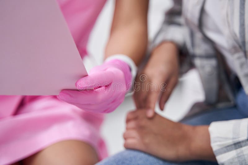 Main femelle dans gants stériles roses dossier d'attente. Une femme tient un document ouvert dans les mains près de la main d'une dame en jean et d'une chemise en plaid