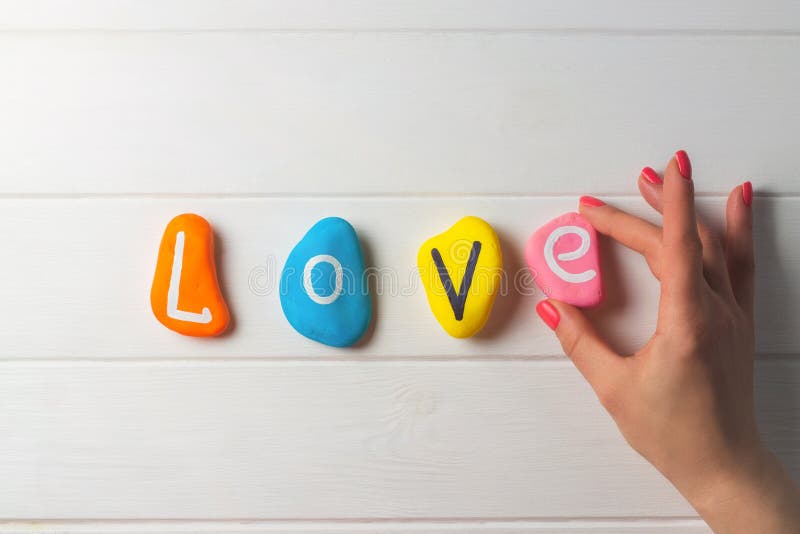 Female hand laying out text Love written on colored pebbles on white wooden surface. Flat lay, copy space. Female hand laying out text Love written on colored pebbles on white wooden surface. Flat lay, copy space