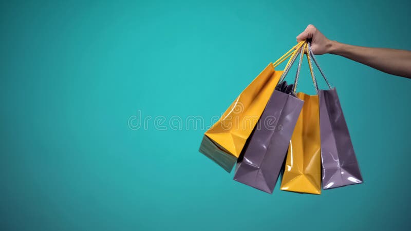 Main femelle tenant beaucoup de sacs ? provisions color?s sur le fond bleu, calibre image libre de droits Main femelle tenant beaucoup de sacs ? provisions color?s sur le fond bleu, calibre image libre de droits
