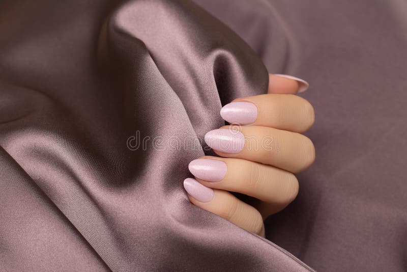 Main féminine avec la conception de l'ongle rose. Manucure rose de vernis à ongles scintillante sur le fond pourpre de tissu