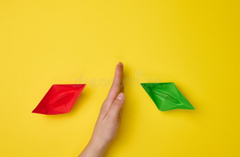 Female hand between paper boats on a yellow background, the concept of reconciliation of the parties, the search for compromises. The role of the negotiator in the dialogue. Female hand between paper boats on a yellow background, the concept of reconciliation of the parties, the search for compromises. The role of the negotiator in the dialogue.