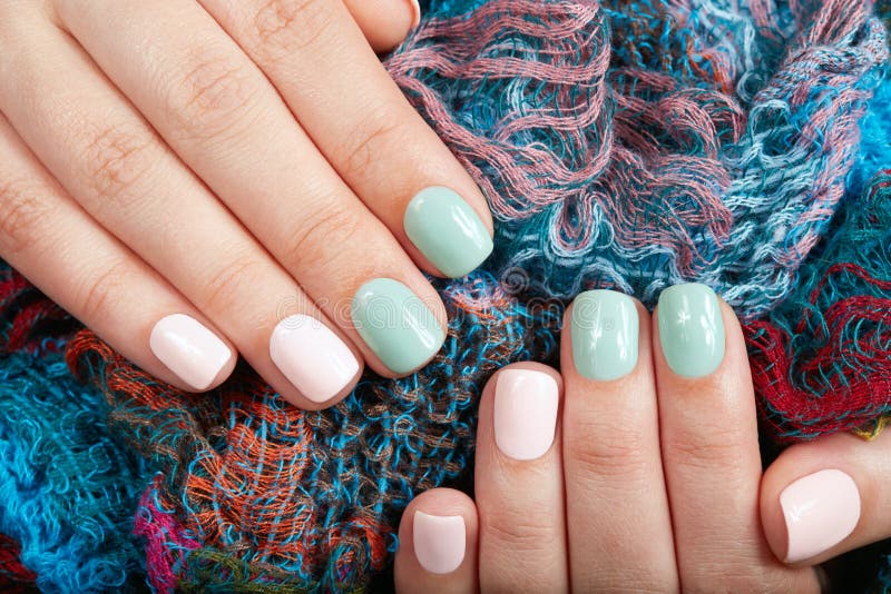 Hands with short manicured nails colored with pink and green nail polish on textile background. Hands with short manicured nails colored with pink and green nail polish on textile background