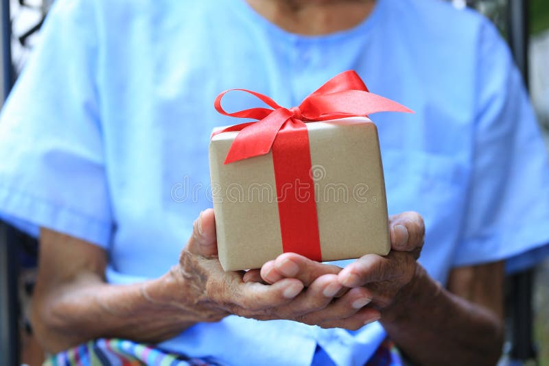 Mains d'homme supérieur tenant le boîte-cadeau avec le ruban rouge pour le jour de Noël et de nouvelle année ou saluant la saison images stock Mains d'homme supérieur tenant le boîte-cadeau avec le ruban rouge pour le jour de Noël et de nouvelle année ou saluant la saison images stock
