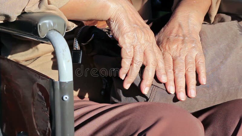 Mains de femme agée sur un fauteuil roulant banque de vidéos