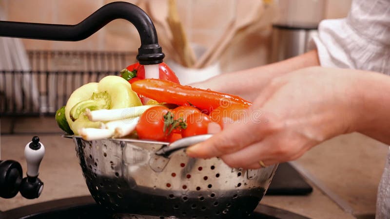 Mains de femme lavant un bon nombre de légumes à l'évier de cuisine banque de vidéos