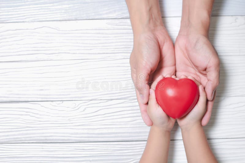Mains de l'homme et du fils tenant le coeur rouge sur le fond en bois photo libre de droits Mains de l'homme et du fils tenant le coeur rouge sur le fond en bois photo libre de droits