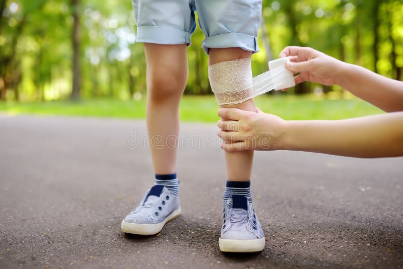 Mains de mère appliquant le bandage médical antibactérien sur le genou de l'enfant après être tombé vers le bas image libre de droits Mains de mère appliquant le bandage médical antibactérien sur le genou de l'enfant après être tombé vers le bas image libre de droits