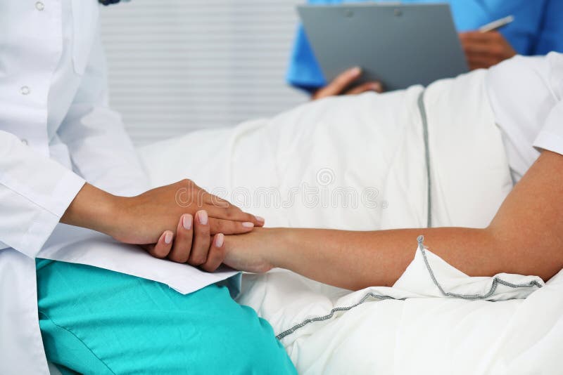 Friendly female doctor hands holding patient hand lying in bed for encouragement, empathy, cheering and support while medical examination. Bad news lessening, compassion, trust and ethics concept. Friendly female doctor hands holding patient hand lying in bed for encouragement, empathy, cheering and support while medical examination. Bad news lessening, compassion, trust and ethics concept