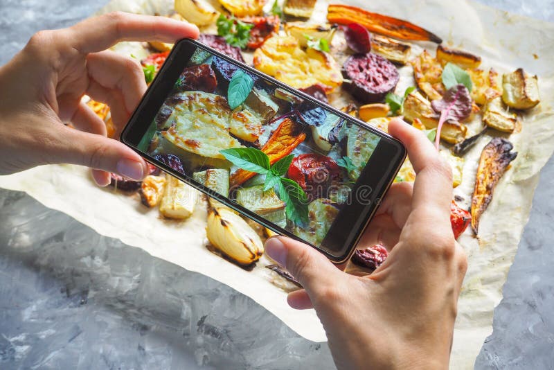 Mains femelles prenant la photo de la nourriture avec le téléphone portable Légumes cuits au four sur le parchemin photographie stock libre de droits Mains femelles prenant la photo de la nourriture avec le téléphone portable Légumes cuits au four sur le parchemin photographie stock libre de droits