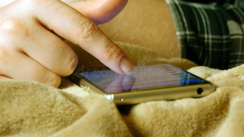 Mains femelles touchant le smartphone tout en se trouvant sur le drap images libres de droits Mains femelles touchant le smartphone tout en se trouvant sur le drap images libres de droits