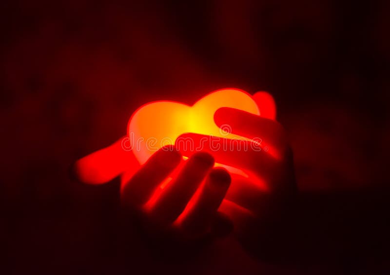 Mains humaines tenant le coeur rougeoyant rouge dans l'obscurité photographie stock Mains humaines tenant le coeur rougeoyant rouge dans l'obscurité photographie stock