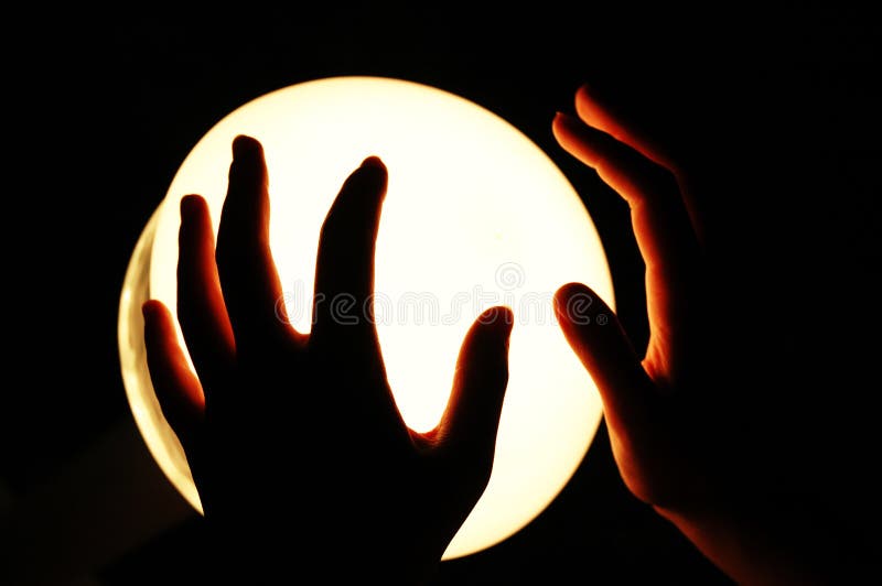 Two hands are silhouetted as they are held over a glowing, lighted round globe. Two hands are silhouetted as they are held over a glowing, lighted round globe.
