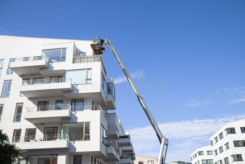 Maintenance workers working at heights from an articulated  boom lift, repairing facade of residential building.