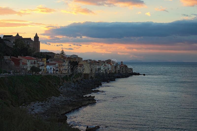 Maisons de Cefalu de village sur les falaises et les vagues se brisant des roches au coucher du soleil La Sicile, Italie photographie stock Maisons de Cefalu de village sur les falaises et les vagues se brisant des roches au coucher du soleil La Sicile, Italie photographie stock