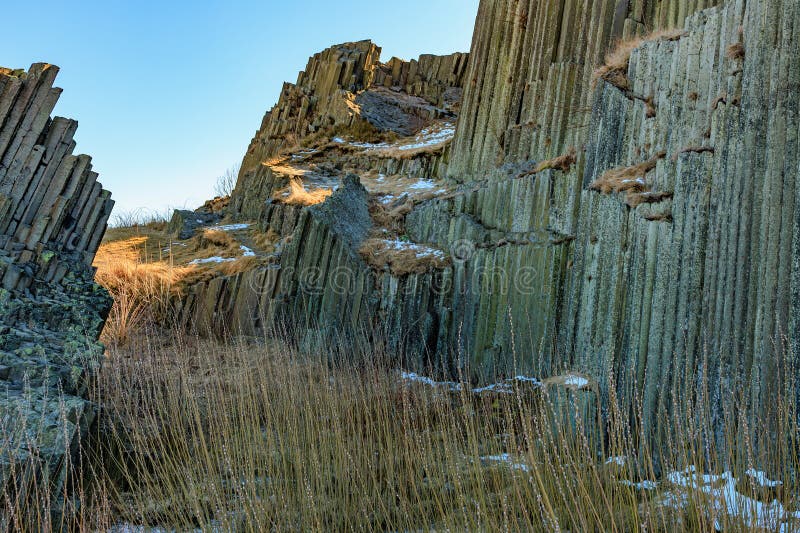 Majestic basalt columns in sunny landscape with snow and grasses stock images