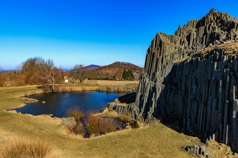 Majestic basalt rock formation beside tranquil lake under clear blue sky stock photography