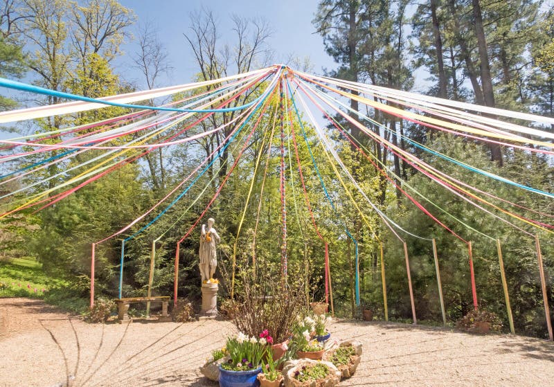 Maypole painted pole, decorated with colored ribbons , around which people dance to celebrate May Day, sunny blue sky Berkshires Massachusetts, flower pots. Maypole painted pole, decorated with colored ribbons , around which people dance to celebrate May Day, sunny blue sky Berkshires Massachusetts, flower pots