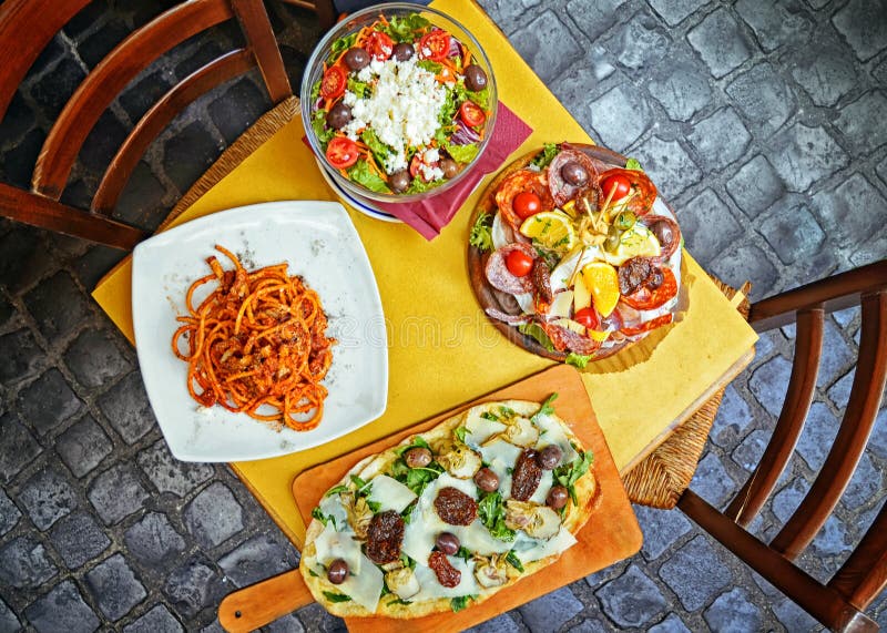A summer dinner .Pasta , pizza , salad and homemade food arrangement in a restaurant Rome .Tasty and authentic Italian food , top view. A summer dinner .Pasta , pizza , salad and homemade food arrangement in a restaurant Rome .Tasty and authentic Italian food , top view