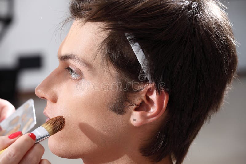 Makeupkonstnär som applicerar fundamentet med en borste, man i klänningen arkivbild Makeupkonstnär som applicerar fundamentet med en borste, man i klänningen arkivbild