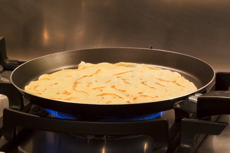 Cooking a delicious crepe made with egg milk flour on a non-stick pan, on a gas flame. In the background satin inox steel. Cooking a delicious crepe made with egg milk flour on a non-stick pan, on a gas flame. In the background satin inox steel.