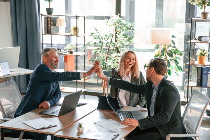 Making High Five, Sitting by the Table. Group of Business People are