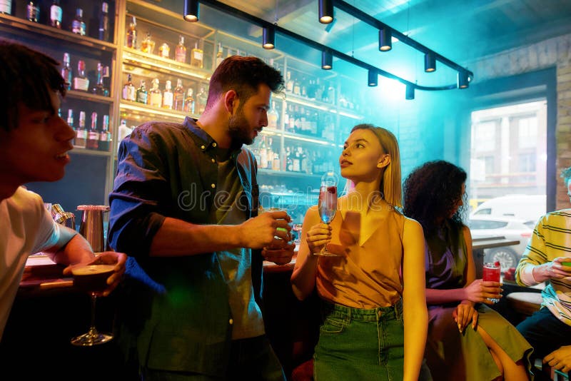 Making night memorable. Young man leaning on bar counter, drinking cocktail and flirting with woman he just met. Young