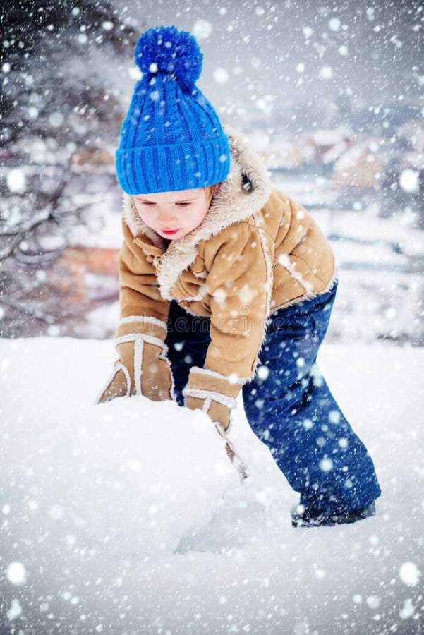 Making snowball and winter fun for children. Kid playing with snow in park. Winter portrait of son in snow Garden. Cute