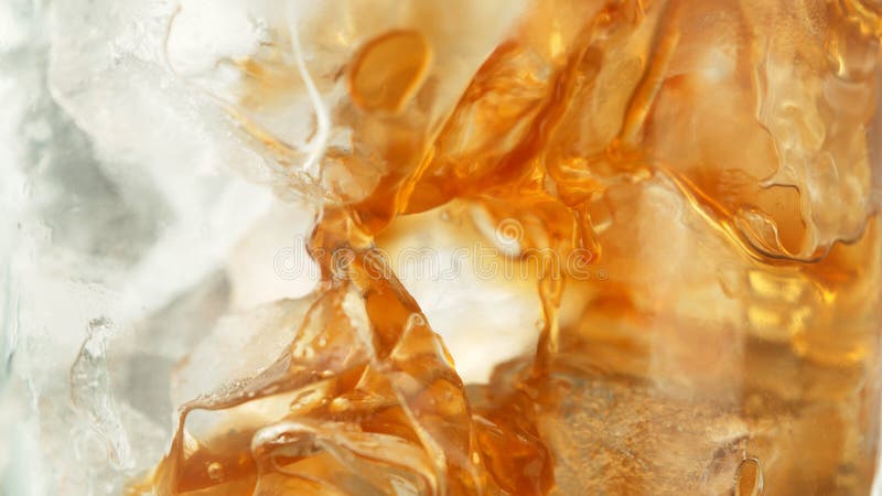 Makroaufnahme des Abgießens brauner Flüssigkeit in Eiswürfel stockfotos