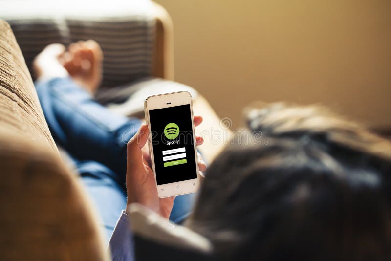 MALAGA, SPAIN - APRIL 26, 2015: Spotify App in a mobile screen hold by woman while lying on a sofa at home.