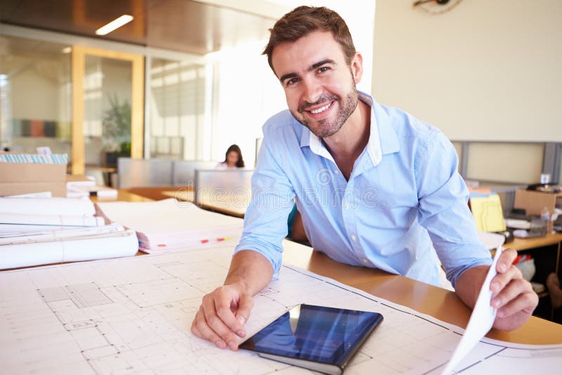 Maschio Architetto Con Tavoletta Digitale Studiare Piani Di Office Sorridente Alla Macchina Fotografica.