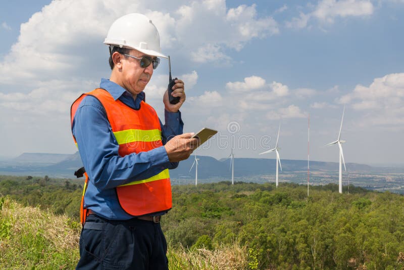 Male Architect or Engineer, use Hand-Held Transceiver Radio and Digital Wireless Tablet Device, working at Wind Turbine Power Generator Field as Infrastructure Construction Project Development. Male Architect or Engineer, use Hand-Held Transceiver Radio and Digital Wireless Tablet Device, working at Wind Turbine Power Generator Field as Infrastructure Construction Project Development