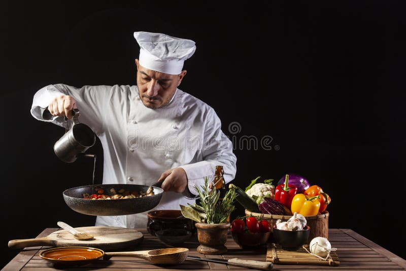 Male chef in white uniform and hat pouring olive oil onto cooking pan with vegetables