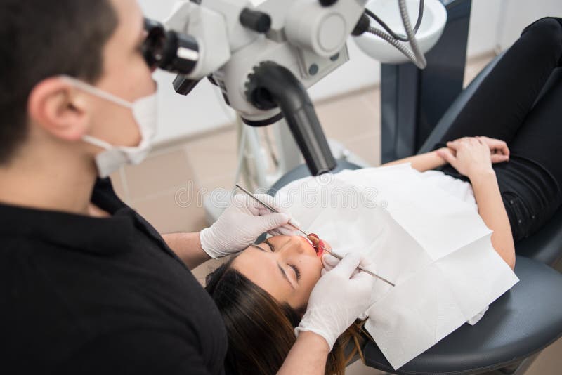 Male dentist with dental tools - microscope, mirror and probe treating patient teeth at dental clinic office stock photo Male dentist with dental tools - microscope, mirror and probe treating patient teeth at dental clinic office stock photo