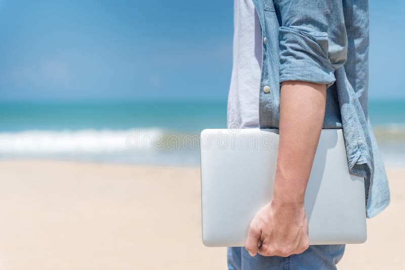 Masculino mano posesión computadora portátil sobre el Playa, en negocios externo en el verano estación, nómadas hombre estilo de vida conceptos.