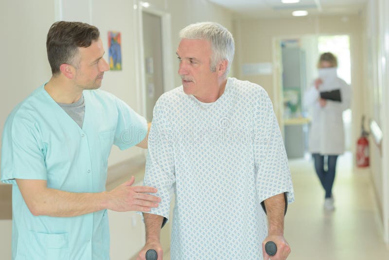 Male doctor helping older patient with crutches.