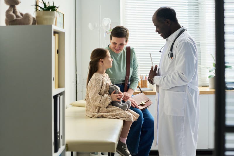 Doctor Conversing with Child and Parent in Clinic Room stock images
