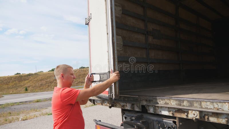 Male driver closing rear door of the truck at countryside. Lorry parked at country road at sunny day. Beautiful