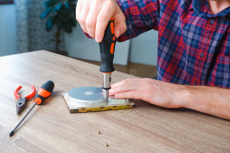 Male engineer repairman disassembles computer hard drive with a screwdriver. Concept of repairing, upgrade, service, electronics royalty free stock image