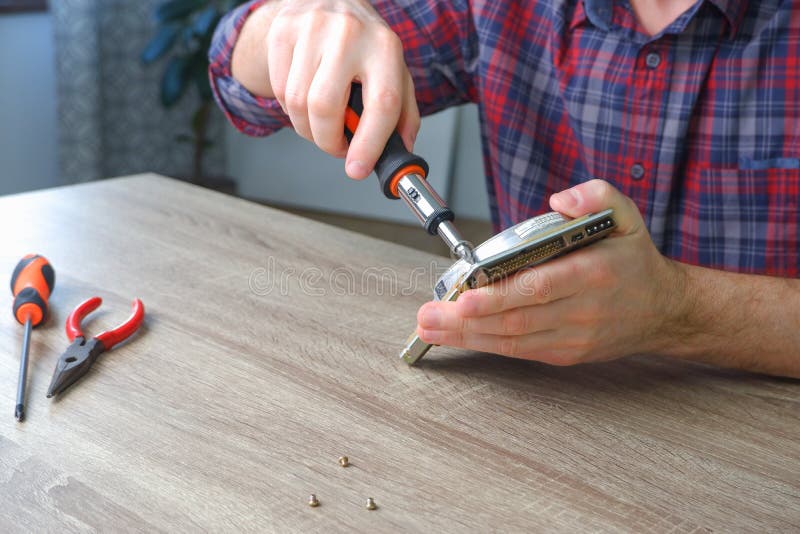 Male engineer repairman disassembles computer hard drive with a screwdriver. Concept of repairing, upgrade, service, electronics stock photo