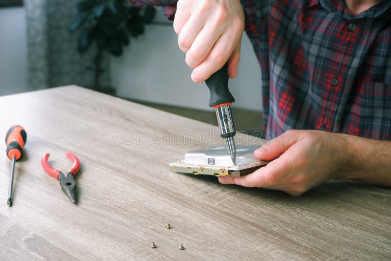 Male engineer repairman disassembles computer hard drive with a screwdriver. Concept of repairing, upgrade, service, electronics royalty free stock image