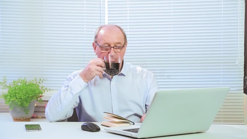 Male executive with glasses in the office at the computer works and drinks coffee