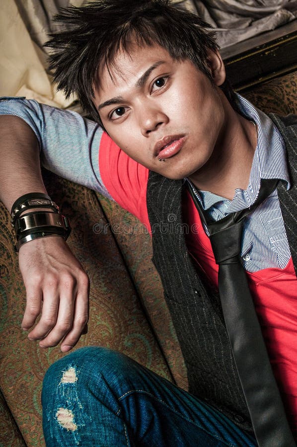 Young guy male model. Asian man with spiked hair in trendy fashion clothing sitting in a night club booth. Wearing suit vest and tie. Oriental, Korean, Vietnamese ethnic young adult. Young guy male model. Asian man with spiked hair in trendy fashion clothing sitting in a night club booth. Wearing suit vest and tie. Oriental, Korean, Vietnamese ethnic young adult.