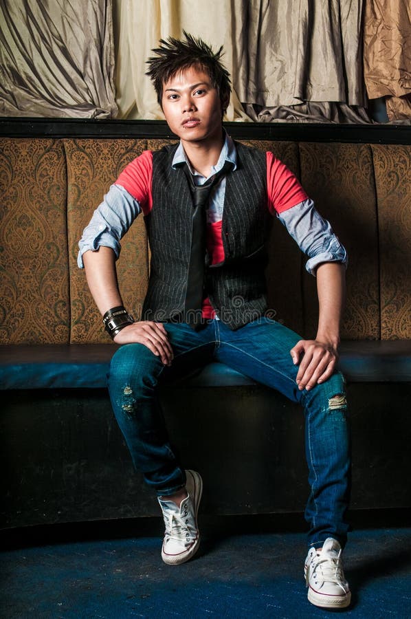Young guy male model. Asian man with spiked hair in trendy fashion clothing sitting in a night club booth. Wearing suit vest and tie. Oriental, Korean, Vietnamese ethnic young adult. Young guy male model. Asian man with spiked hair in trendy fashion clothing sitting in a night club booth. Wearing suit vest and tie. Oriental, Korean, Vietnamese ethnic young adult.