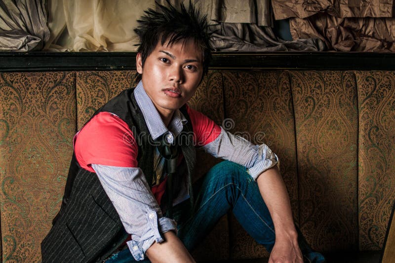 Young guy male model. Asian man with spiked hair in trendy fashion clothing sitting in a night club booth. Wearing suit vest and tie. Oriental, Korean, Vietnamese ethnic young adult. Young guy male model. Asian man with spiked hair in trendy fashion clothing sitting in a night club booth. Wearing suit vest and tie. Oriental, Korean, Vietnamese ethnic young adult.