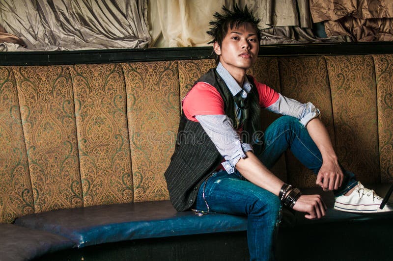 Young guy male model. Asian man with spiked hair in trendy fashion clothing sitting in a night club booth. Wearing suit vest and tie. Oriental, Korean, Vietnamese ethnic young adult. Young guy male model. Asian man with spiked hair in trendy fashion clothing sitting in a night club booth. Wearing suit vest and tie. Oriental, Korean, Vietnamese ethnic young adult.